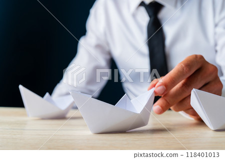 Businessman placing paper made origami boat on wooden desk Businessman placing paper made origami boat on wooden desk 118401013