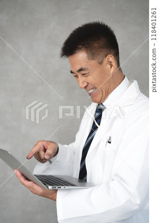 Senior man in a white coat standing and using a laptop Senior man in a white coat standing and using a laptop 118401261