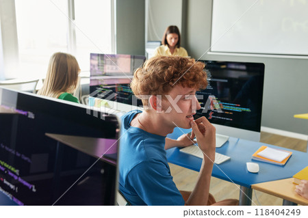 Side view portrait of red haired young man talking to friend during IT class in school or college with teacher in background 118404249