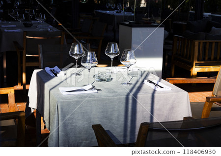 There is a table with three wine glasses and silverware set on it 118406930