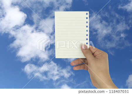 Hand holding a empty note paper with a background of blue sky and white clouds. Hand holding a empty note paper with a background of blue sky and white clouds. 118407031