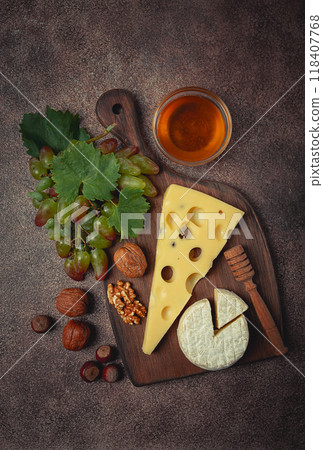 cheese with big holes, emmental, maasdam, brie cheese, on a cutting board, with grapes and honey, nuts, appetizer to wine, top view, 118407768