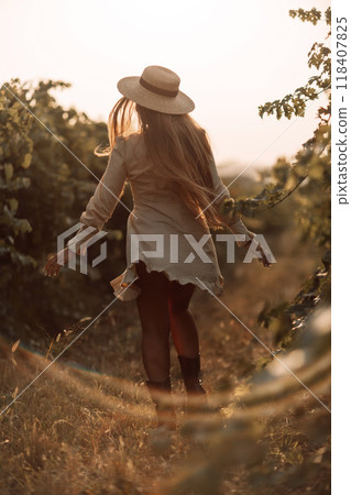 Woman with straw hat stands in front of vineyard. She is wearing a light dress and posing for a photo. Travel concept to different countries 118407825