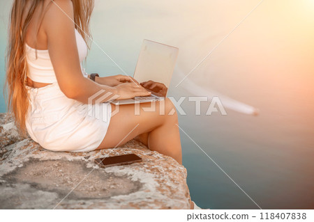 Freelance women sea working on the computer. Good looking middle aged woman typing on a laptop keyboard outdoors with a beautiful sea view. The concept of remote work. 118407838