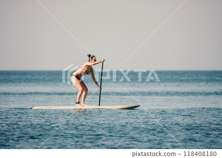 Sea woman sup. Silhouette of happy middle aged tanned woman in rainbow bikini, surfing on SUP board, confident paddling through water surface. Idyllic sunset. Active lifestyle at sea or river. 118408180