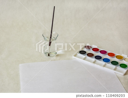 Watercolors, a glass of water with a brush and a sheet of white paper on a light background Watercolors, a glass of water with a brush and a sheet of white paper on a light background 118409203