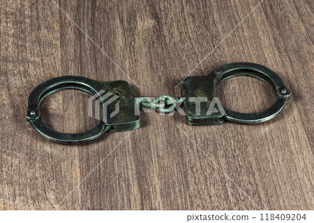 Metal handcuffs lie on a wooden table. On the wooden table lie the metal handcuffs 118409204