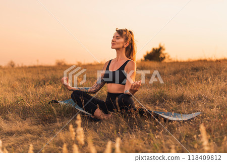 Woman in Lotus Pose on Yoga Mat Outdoors 118409812