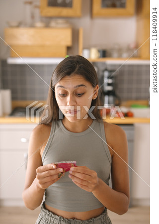A surprised woman carefully examining a package in her bright and modern kitchen space 118409914