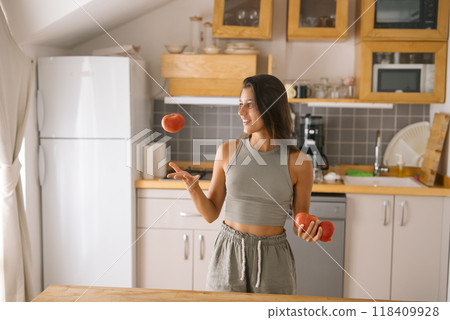 A woman skillfully juggling colorful apples while enjoying a modern kitchen environment 118409928