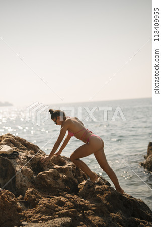 A woman is energetically climbing rocks at the seaside under the warm summer sunlight 118409955