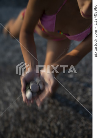 A young girl joyfully collects beautiful seashells along the sandy beach by the ocean A young girl joyfully collects beautiful seashells along the sandy beach by the ocean 118409966