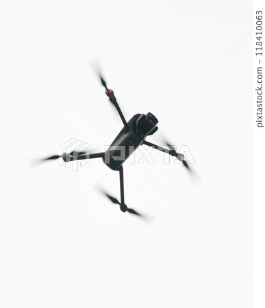 Black Four-Propeller Drone Flying Against Bright Sky Black Four-Propeller Drone Flying Against Bright Sky 118410063