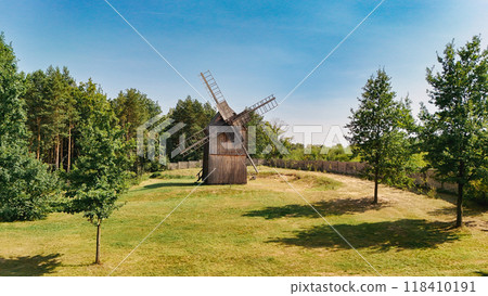 Wooden windmill in an open field surrounded by trees, captured on a sunny day. A perfect example of traditional rural architecture, blending history and nature in a peaceful countryside setting Wooden windmill in an open field surrounded by trees, captured on a sunny day. A perfect example of traditional rural architecture, blending history and nature in a peaceful countryside setting 118410191