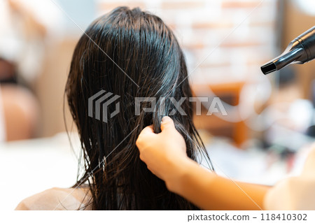 A hairdresser blow-drying a woman's long hair 118410302