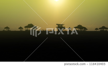 Silhouettes of people enjoying a beach sunset near huts and a lifeguard tower 118410403