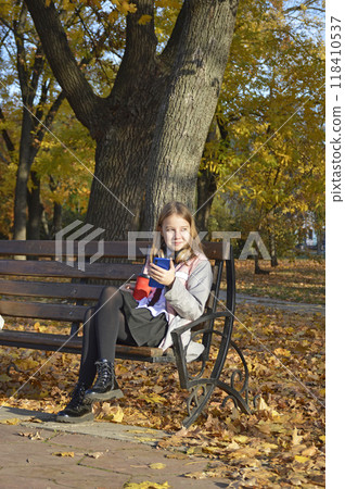 a girl sits on a bench in an autumn park, headphones on her head 118410537