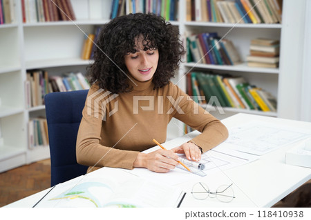 Cute young curly-haired woman sitting at the table in the library Cute young curly-haired woman sitting at the table in the library 118410938