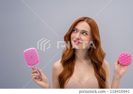 Cute young long-haired woman holding a scalp massager in hands 118410941
