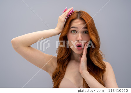 Ginger young woman massaging her head with a scalp massager Ginger young woman massaging her head with a scalp massager 118410950