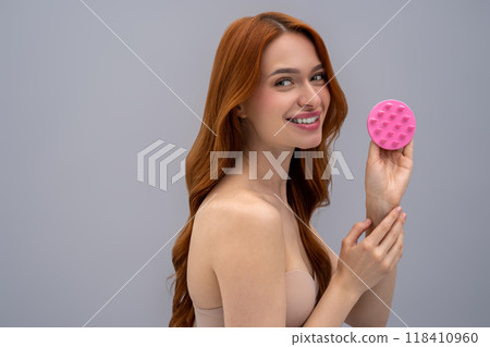 Long-haired caucasian woman on a grey background with a scalp massager in hands 118410960
