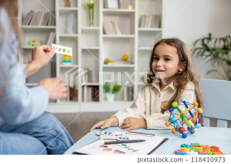 Cute girl having an educational session with a speech therapist and looking involved 118410973