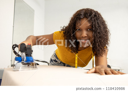 Curly-haired seamstress ironing a new model in her studio 118410986