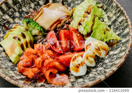 Colorful salad bowl with fresh vegetables, avocado, eggs, and sauce - healthy and vibrant meal 118411049