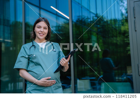 Pregnant young doctor on the clinic building background Pregnant young doctor on the clinic building background 118411205