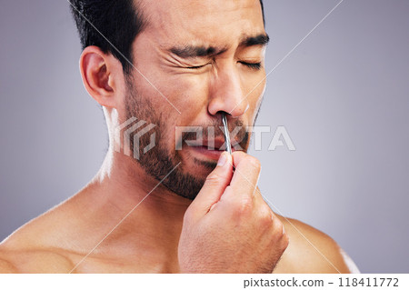 Plucking hair, nose and a man with tweezers for grooming, hygiene and beauty on a studio background. Pain, face and an Asian person with tools for cosmetics or facial care isolated on a backdrop 118411772