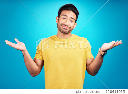 Confused, question and portrait of man shoulder shrugging and raise arms isolated in a blue studio background. Clueless, smile and young male person with doubt, whatever and doing a hand gesture 118411935