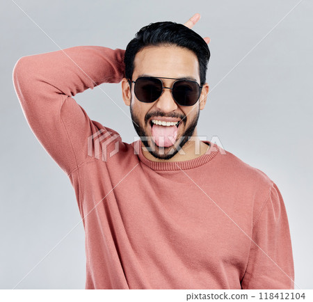 Portrait, tongue out and Asian man with sunglasses, funny and silly against a grey studio background. Face, Japanese male and guy with funky eyewear, shades and comic with humor and goofy expression 118412104