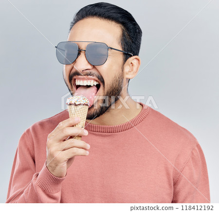 Summer, sunglasses and ice cream with a man in studio on a gray background enjoying a sweet, treat or snack. Food, fashion and dessert with a handsome young male eating or licking an icecream cone 118412192