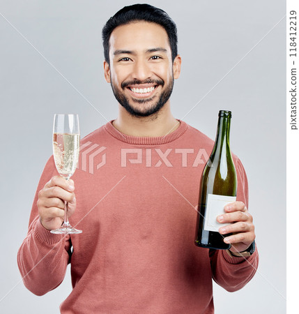 Portrait, champagne and cheers with a man in studio on a gray background holding a bottle for celebration. Glass, alcohol and toast with a handsome young man celebrating the new year tradition Portrait, champagne and cheers with a man in studio on a gray background holding a bottle for celebration. Glass, alcohol and toast with a handsome young man celebrating the new year tradition 118412219