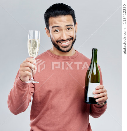 Portrait, champagne and toast with a man in studio on a gray background holding a bottle for celebration. Glass, alcohol and cheers with a handsome young man celebrating the new year tradition 118412220