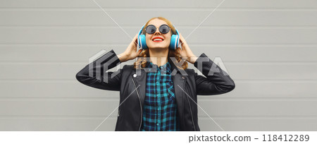 Portrait of happy modern young woman listening to music with headphones on gray background Portrait of happy modern young woman listening to music with headphones on gray background 118412289