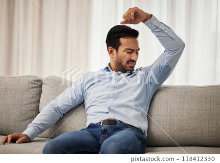 Armpit stink, smelling and a man on the sofa with a hygiene or bacteria problem. Bad, home and an Asian person with body odor, underarm sweat or grooming issue on the living room couch after work 118412330