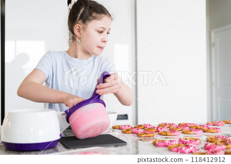 With focused attention, this budding culinary artist dips pretzels into a pot of melted chocolate, creating sweet delights in the warmth of a well-lit home kitchen. With focused attention, this budding culinary artist dips pretzels into a pot of melted chocolate, creating sweet delights in the warmth of a well-lit home kitchen. 118412912