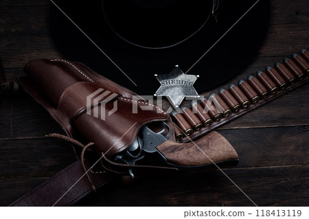 Old west sheriff star badge with gun, holster and gun belt with old west hat on table. Top view. Old west sheriff star badge with gun, holster and gun belt with old west hat on table. Top view. 118413119
