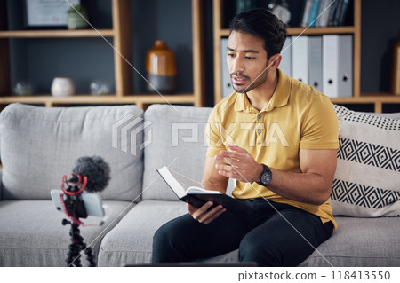 Podcast, bible study and phone with a man online to preach or reading while live streaming. Asian male on home sofa with Christian scripture or book as content creator teaching on education religion Podcast, bible study and phone with a man online to preach or reading while live streaming. Asian male on home sofa with Christian scripture or book as content creator teaching on education religion 118413550