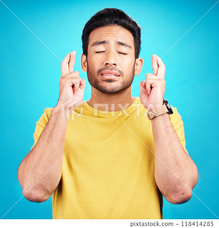 Hope, man and fingers crossed for luck in studio isolated on a blue background. Wish, hand gesture and male person with aspiration, hoping emoji and wait for good fortune, result or optimistic faith. Hope, man and fingers crossed for luck in studio isolated on a blue background. Wish, hand gesture and male person with aspiration, hoping emoji and wait for good fortune, result or optimistic faith. 118414285