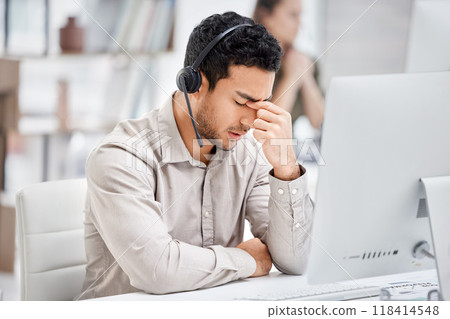 Mental health, man with headache and headset at his desk with computer in a modern workplace office. Telemarketing or call center, sad or burnout and male person tired or depressed at his workstation 118414548