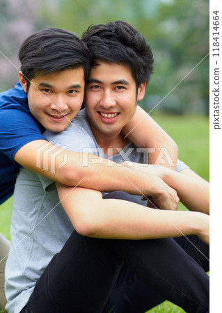 Asian men, gay couple and hug in park portrait, grass or garden with love, care and bonding in summer sunshine. Happy Japanese guy, romance or relax together on lawn with lgbtq, nature and holiday 118414664
