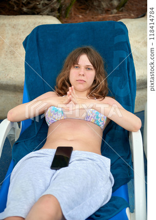 Relaxing Summer Vacation: Teenage Girl Lounging on Sunbed in Mediterranean Paradise with Palm Trees and Blue Sky. Idyllic Mediterranean Getaway: Sunny Mediterranean Escape: 14-Year-Old Girl Relaxing Relaxing Summer Vacation: Teenage Girl Lounging on Sunbed in Mediterranean Paradise with Palm Trees and Blue Sky. Idyllic Mediterranean Getaway: Sunny Mediterranean Escape: 14-Year-Old Girl Relaxing 118414784