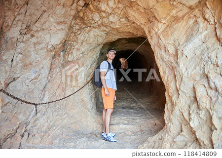 Daring Young Adventurer Poised at Threshold of Enigmatic Cave System Inviting Exploration of Untamed Wilderness 118414809