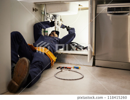 Kitchen, maintenance and renovation with a plumber on the floor of a home to fix a leak, issue or problem. Plumbing, repair and tools with a handyman or contractor working on a pipeline in a house 118415260
