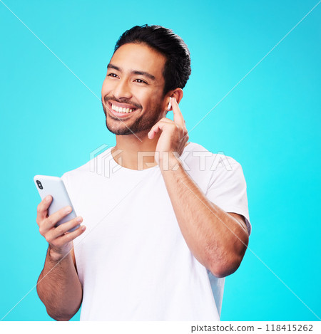 Asian man, earphones and smartphone in studio for music, podcast app and blue background. Happy male model thinking with mobile phone, listening to audio and streaming sound of radio media with tech 118415262