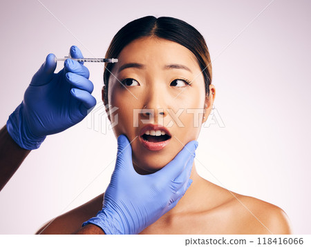 Woman, needle and fear on face in studio for surgery, cosmetics and shock with collagen by white background. Japanese patient, doctor and syringe for dermatology, change and pain for skin aesthetic 118416066