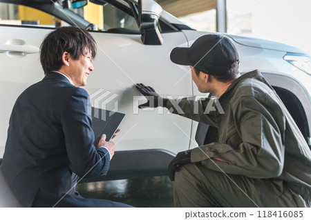A male mechanic and a salesman in a suit checking scratches and dents on a car A male mechanic and a salesman in a suit checking scratches and dents on a car 118416085