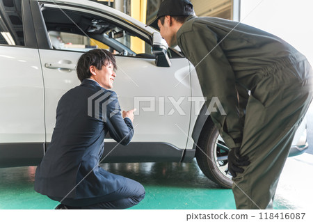 A male mechanic and a salesman in a suit checking scratches and dents on a car A male mechanic and a salesman in a suit checking scratches and dents on a car 118416087